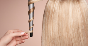 a women giving curls to the hair of another women while holding curler downwards and rotating hair on rod